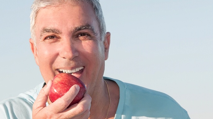 man holding an apple and enjoying the benefits of dentures in Philadelphia