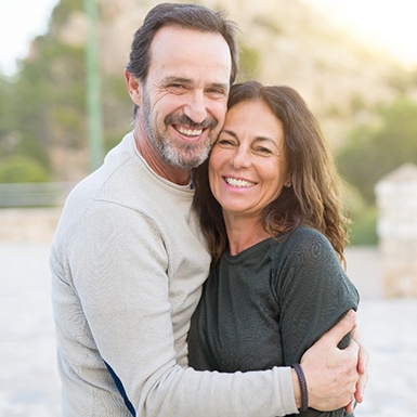 Older couple with dental implants in Philadelphia hugging outside