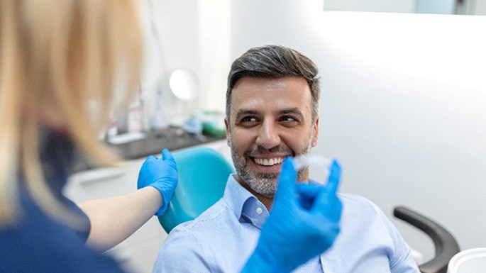 Man smiling at dental assistant holding Invisalign aligner