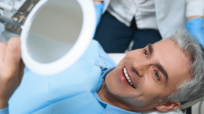 A smiling man looking at his dental veneers in Philadelphia