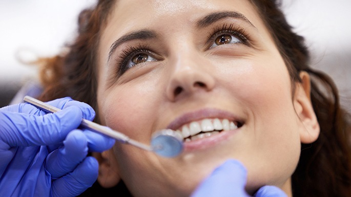 A person smiling while a dentist examines their mouth before dental implant placement