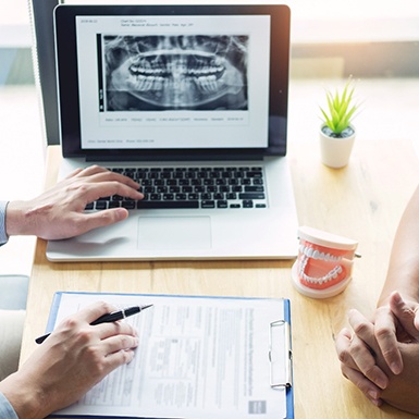 A dentist and patient examining dental x-rays on laptop