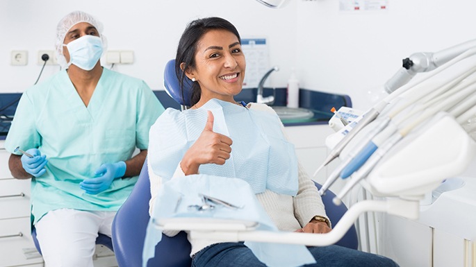 a dental patient giving a thumbs-up in a treatment chair
