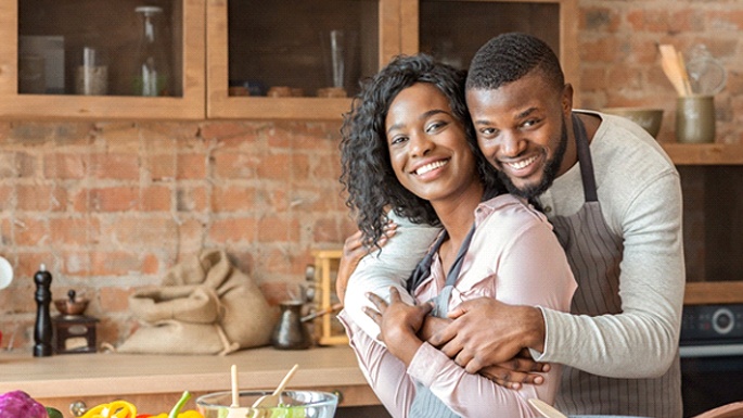 A young couple hugging in the kitchen and cooking together after seeing their Cigna dentist in Philadelphia