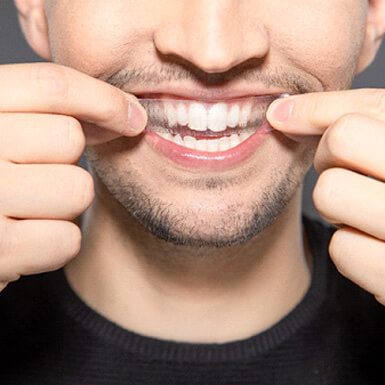 A man placing a whitening strip on his teeth