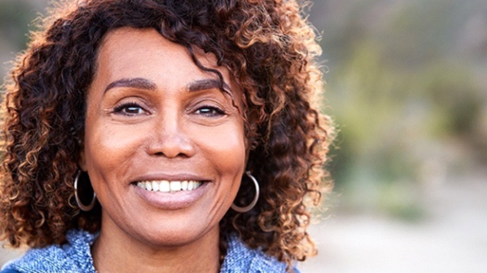 Smiling woman with dental implant tooth replacement in a blue jacket