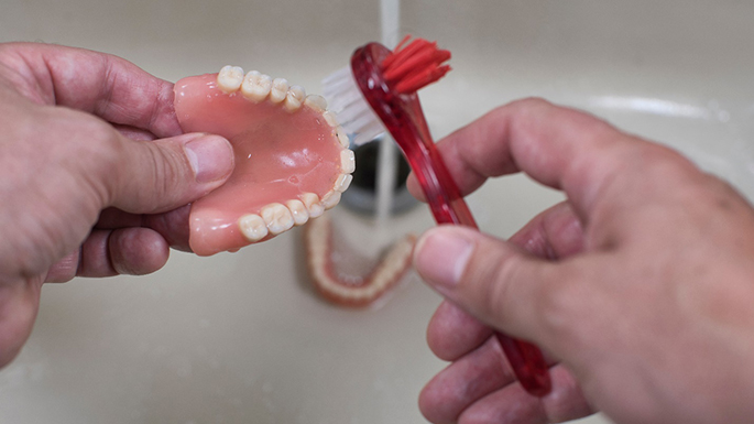 hands cleaning removeable dentures with a brush