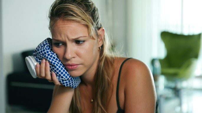 Woman in need of emergency dentistry holding ice pack to cheek