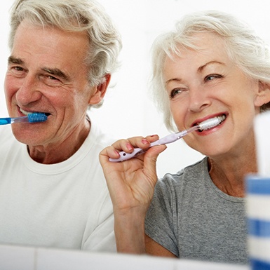 older couple brushing teeth together in bathroom 