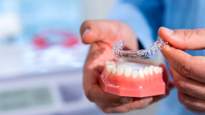 Dentist placing clear aligner on model of teeth