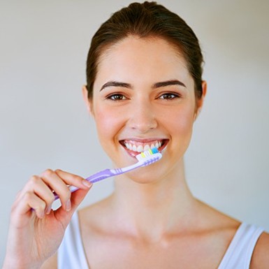 a woman smiling while brushing her teeth