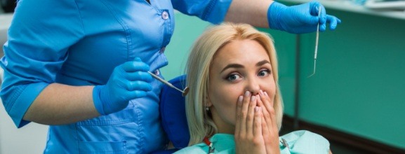 Woman in need of emergency dentistry covering her smile
