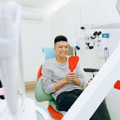 Smiling man in dentist’s chair looking in mirror