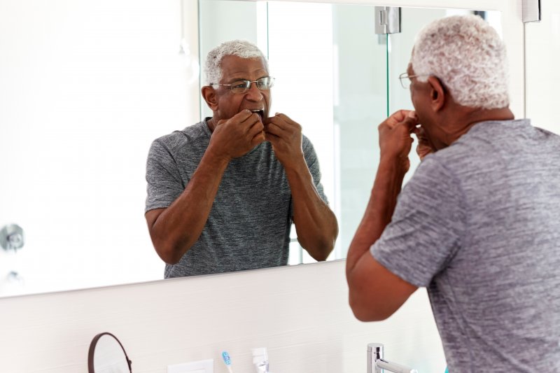 Man flossing dental implants in Philadelphia in his bathroom