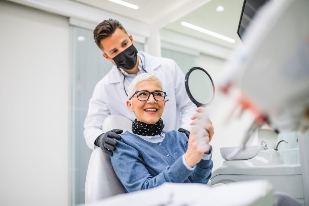 Woman in dental chair smiling at reflection in mirror with dentist behind her
